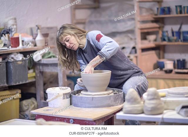 Female potter shaping clay pot on pottery wheel