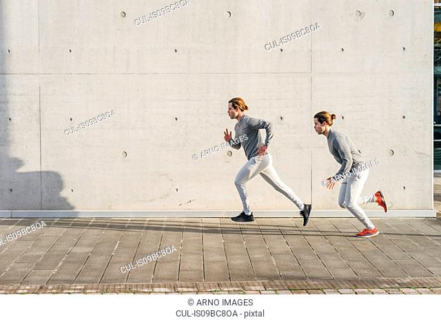Young adult male twins running together, running up sidewalk