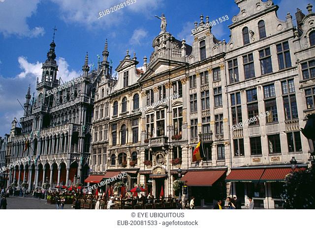 Grand Place. Maison du Roi on left beside decorative facades of old town buildings busy outside tables of cafe and people crossing square