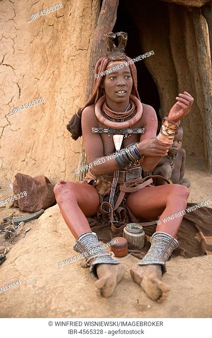Himba woman with child in front of the hut, rubs itself with Okra, butterfat with ochre paint, Kaokoveld, Namibia