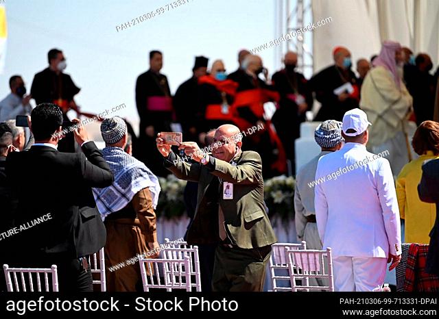 06 March 2021, Iraq, Nasiriyah: A spectator at the papal visit takes a selfie with Pope Francis in the background. Francis is visiting the Sumerian city-state...