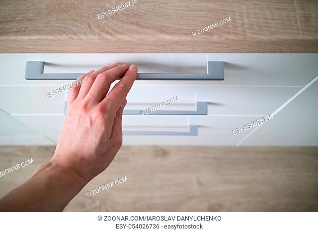 The man hand is open is in the white kitchen cabinet with drawer