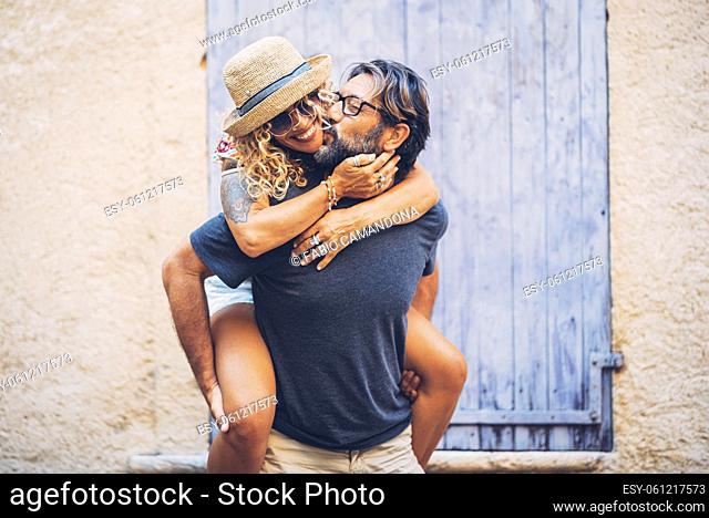 Carefree couple spending leisure time together outdoors, man giving piggyback ride to cheerful tattooed woman in sunglasses and straw hat