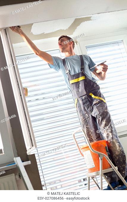 Thirty years old manual worker with wall plastering tools renovating house. Plasterer renovating indoor walls and ceilings with float and plaster