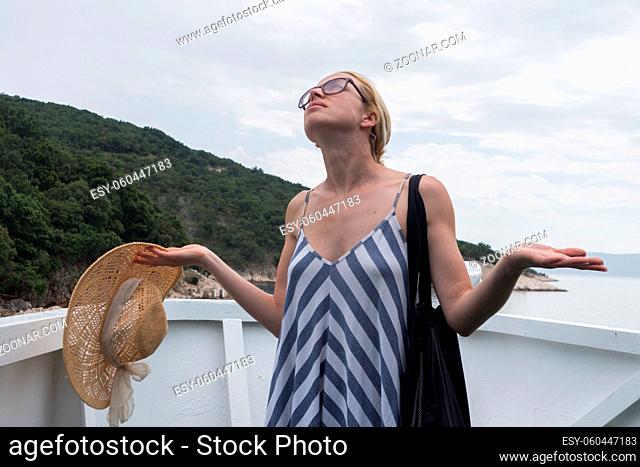 Disappointed female tourist on summer cruss ship vacation, standing on rain and looking angry at overcast cloudy sky. Allways take the weather with you on...