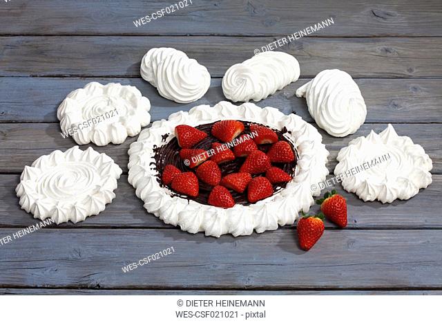 Meringues and meringue baked pastry case with chocolate icing garnished with strawberries on grey wood