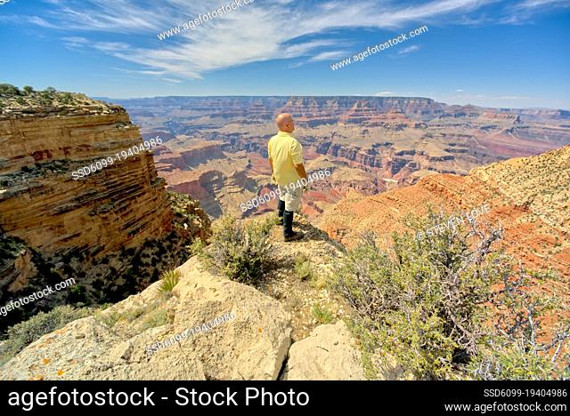 A man standing on a cliff overlooking Grand Canyon South Rim Arizona east of Moran Point