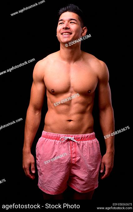 Studio shot of young handsome muscular multi ethnic man shirtless against black background