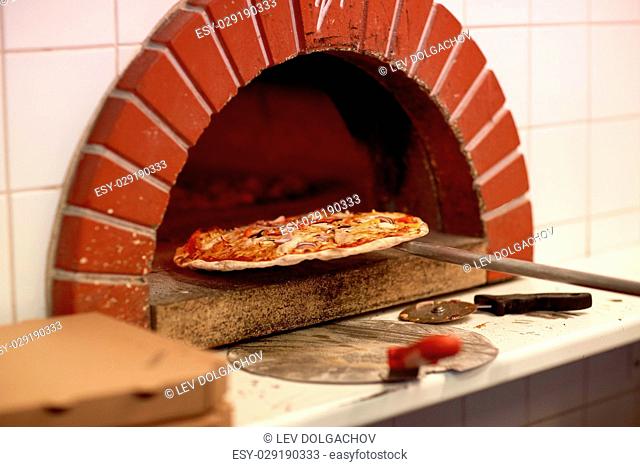 food, italian kitchen and cooking concept - peel taking baked pizza out of oven at pizzeria