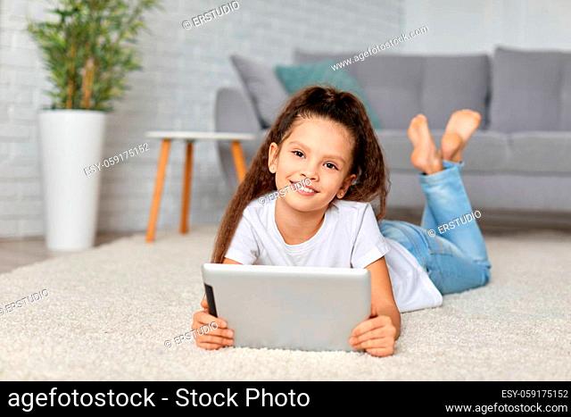 smiling little child girl lying on the carpet and using digital tablet at home. kid enjoying tablet