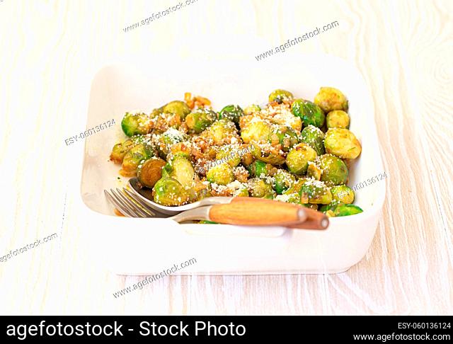 Healthy vegetarian dish roasted brussels sprouts with butter and parmesan cheese in white ceramic casserole close up on wooden table angle view, vegan food