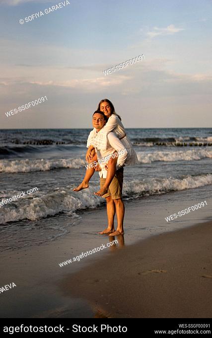 Boyfriend giving girlfriend piggyback ride at beach on sunset