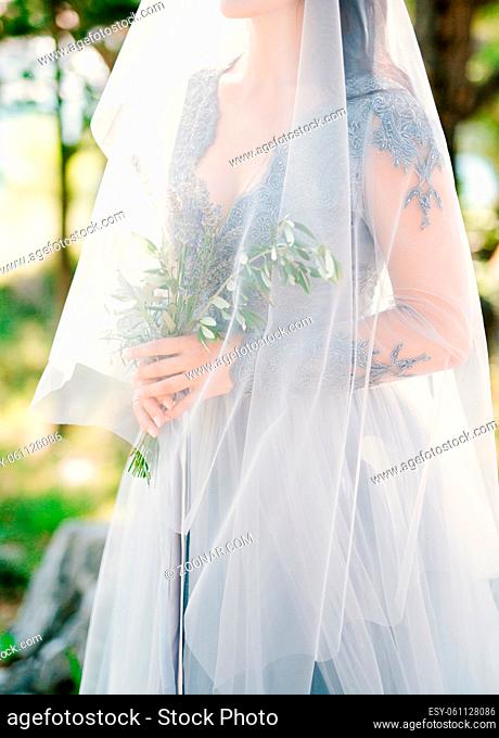 Lavender Wedding bouquet in hands of the bride under veil in pale blue dress