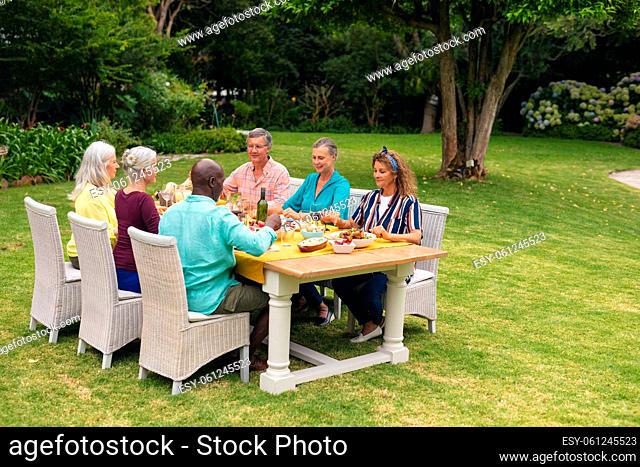 Multiracial senior male and female friends having food at table during backyard party