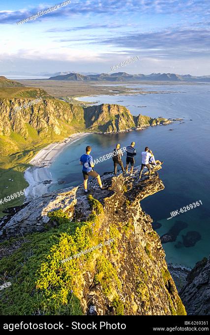 Four hikers standing on rocky outcrop, view of rocks, beach and sea, summit of Måtinden mountain, near Stave, Nordland, Norway, Europe