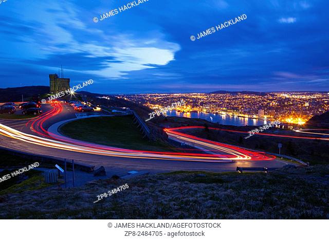 Light trails created by cars as they zip up and down Signal Hill with St. John's and its harbour in the background at dusk. Newfoundland, Canada