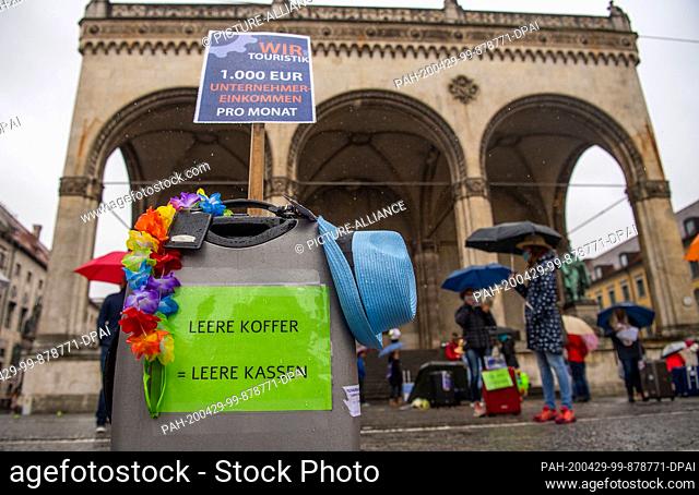 29 April 2020, Bavaria, Munich: ""Empty suitcases, empty coffers"" is written on a suitcase decorated with a garland and a Fedora hat