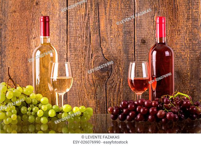 Glasses of wine with bottles and grapes in front of wooden background dark background