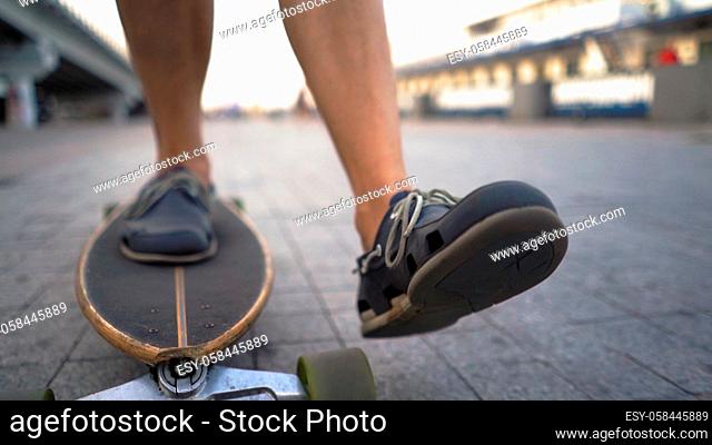 The Skater's Legs Are Accelerated On A Longboard Forward On A Flat City Road. Close-Up