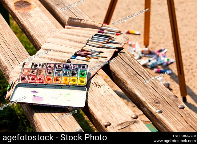 Set of professional art supplies outside in sunny day. Art palette, watercolors and brushes on a bench