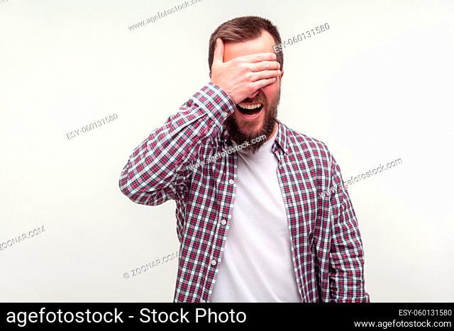 Don't want to look. Portrait of astonished bearded man in casual plaid shirt has eyes closed with hand and mouth open in surprise