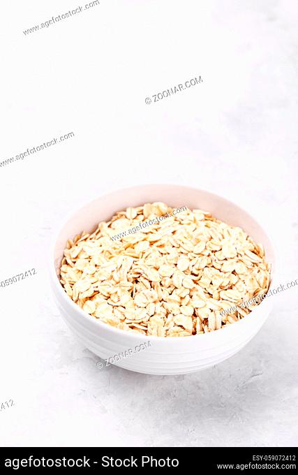 Old fashioned rolled oats in a white bowl on grey stone table