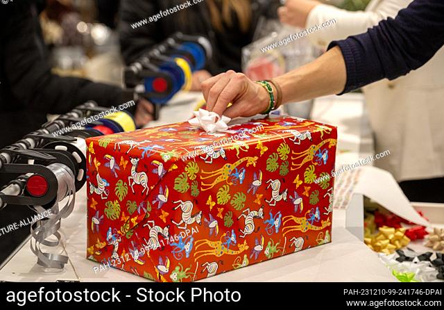 PRODUCTION - 09 December 2023, Baden-Württemberg, Ulm: A sales clerk wraps a Christmas present for customers in a department store