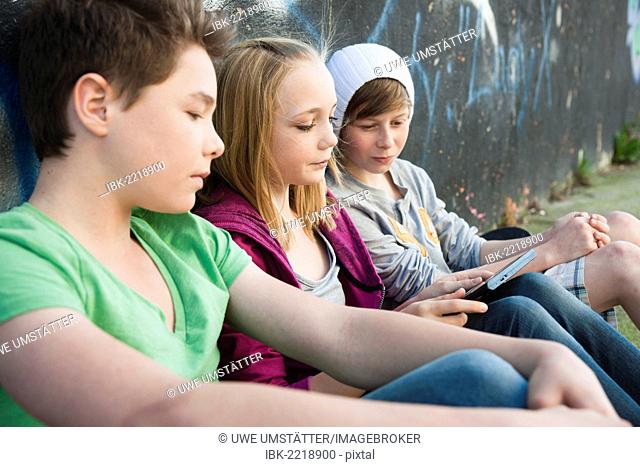 Three teenagers with a tablet PC sitting in front of a wall with graffiti