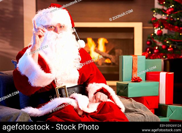 Portrait of Santa Claus by fireplace raising pointing finger, looking at camera