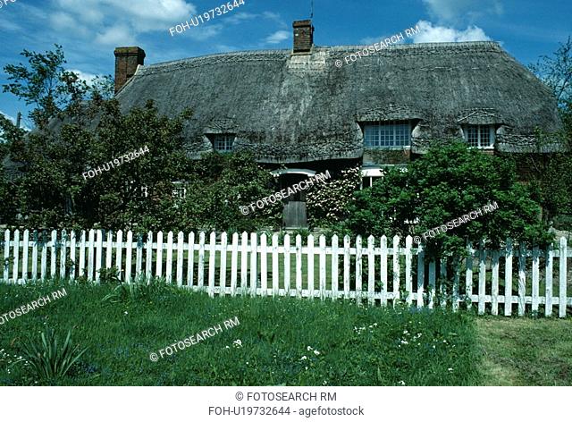 White picket fence in front of country cottage with thatched roof