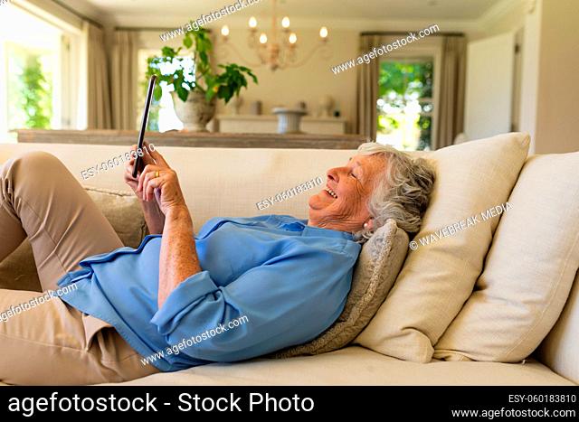Senior caucasian woman lying on sofa using tablet
