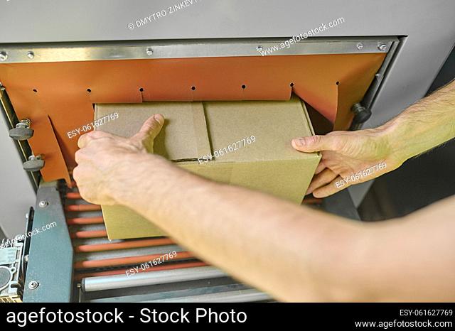 Cropped photo of operator hands putting the cardboard box on the conveyor rollers of the carton sealing machine