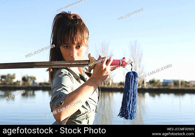 Intense female martial artist holding sword against her face at park on sunny day