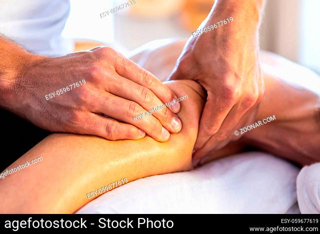 Massage and body care. Woman lying and relaxing at massage in a cosy home environment. Strong hands of professional male masseur doing gentle massage