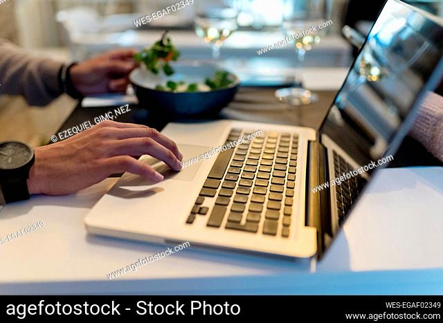 Man using laptop while eating salad at restaurant