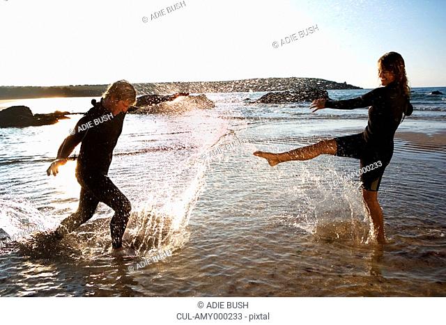 Couple in wetsuits splashing in shallow water