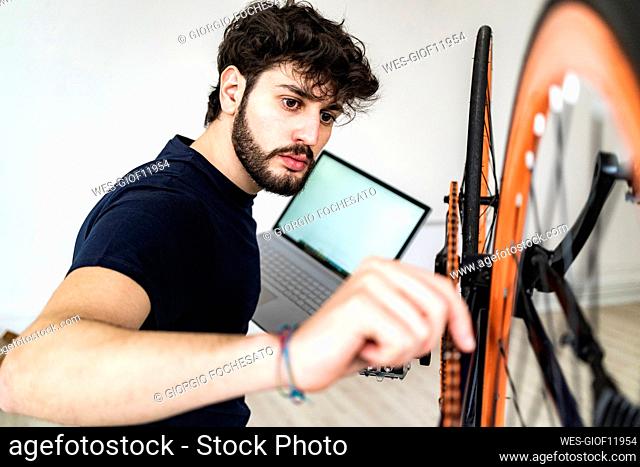 Young man with laptop holding bicycle chain at home