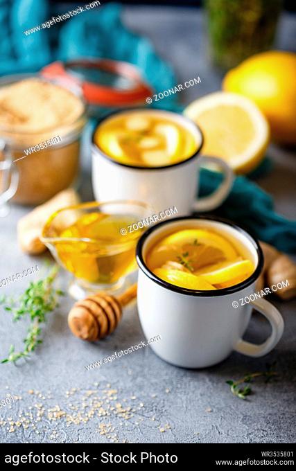 Two enameled cups with ginger-lemon tea, thyme, cinnamon, anise and honey on a gray background. Shallow depth of field