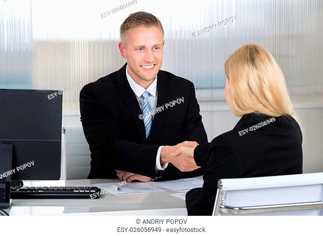 Smiling young businessman shaking hands with female candidate at desk in office