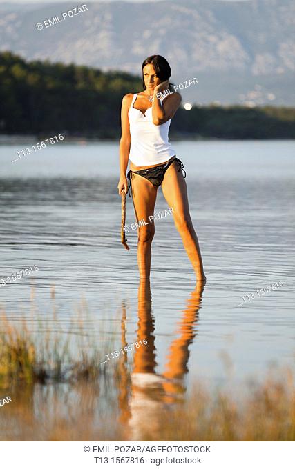 Young woman is standing in a shallow water with a tree branch in hand