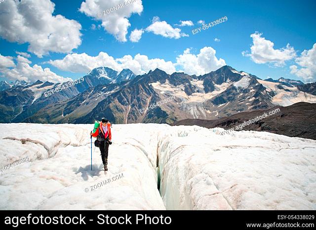 Female mountaineer enjoying the beauty of the glacier walks on the glacier in the crampon and sunglasses. Against the backdrop of the high mountains of the...