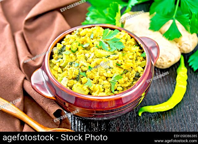 Indian national dish kichari made of mung bean, rice, celery, spinach, hot pepper and spices in a bowl on a towel, ginger and spoon on wooden board background