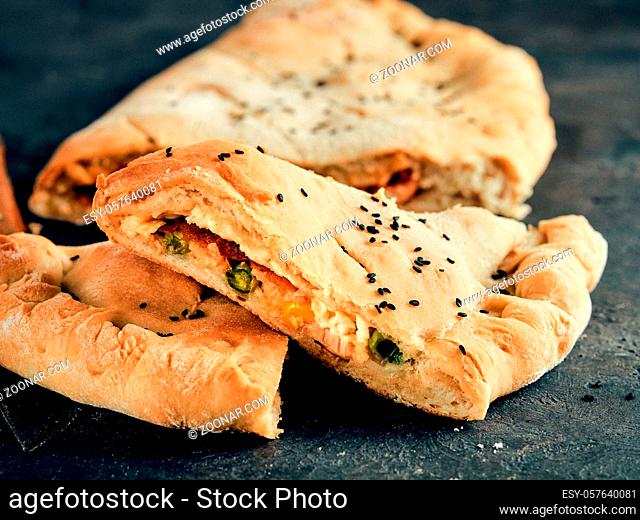 Perfect homemade closed pizza calzone on baking paper sheets over black background. Cutting tasty italian closed calzone pizza with cheese, meat, vegetables