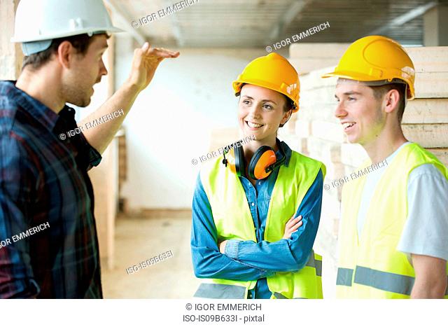 Three people standing in constructions site, wearing hard hats, having discussion