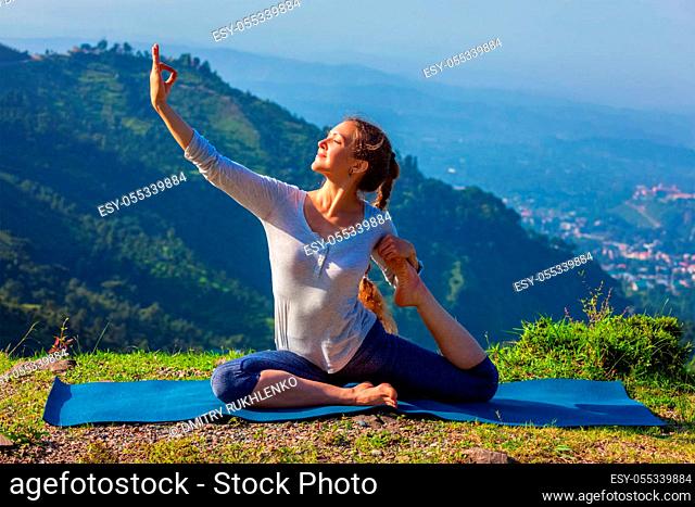 Yoga outdoors - young sporty fit woman doing stretching yoga asana Eka pada rajakapotasana - one-legged king pigeon pose in Himalayas mountains, India