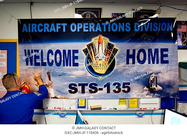 NASA astronaut Doug Hurley, STS-135 pilot, signs a welcome home banner before a ceremony for the Atlantis crew on July 22, 2011 at Ellington Field in Houston