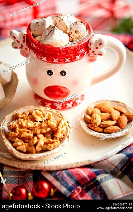Delicious homemade christmas hot chocolate or cocoa with marshmellows in a red xmas decorative cup. With almonds, walnuts in small bowls on side