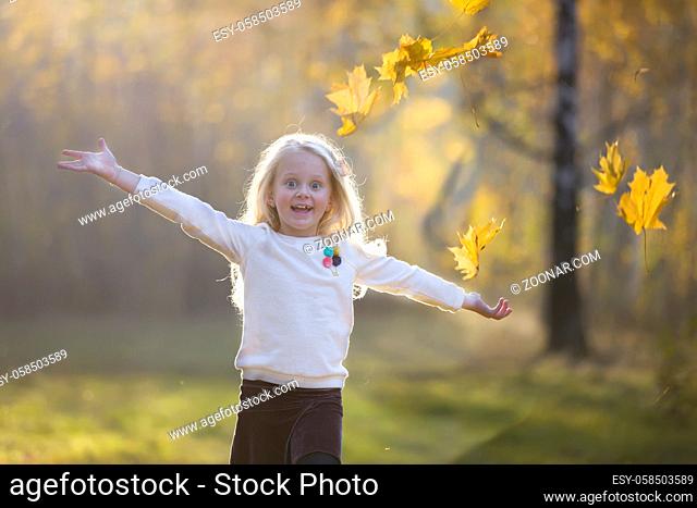 A girl in the autumn park scatters maple leaves. A child on a walk in the fall