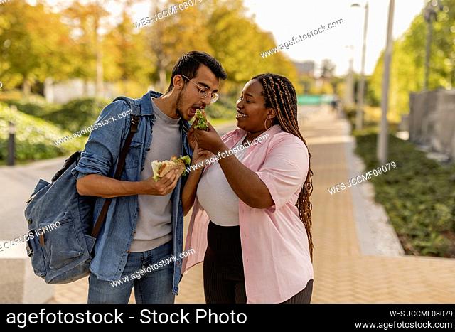Young woman sharing sandwich with boyfriend at footpath