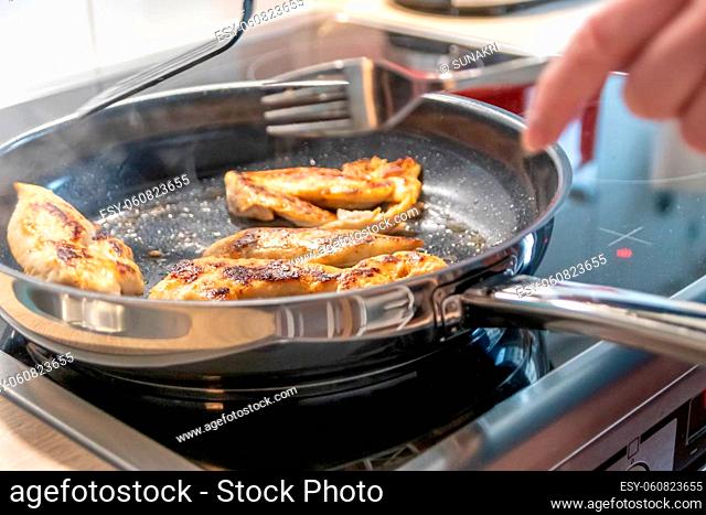 Woman cooking and frying chicken breasts and chicken filet in a pan on an hot stove in the kitchen as delicious meal and diet dinner cuisine for healthy...